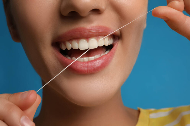 Young woman flossing her teeth on blue background, closeup. Cosmetic dentistry - Foto, immagini