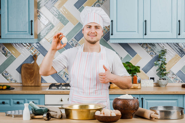 hombre en un delantal en la cocina señala con el dedo los huevos de pollo. - Foto, imagen