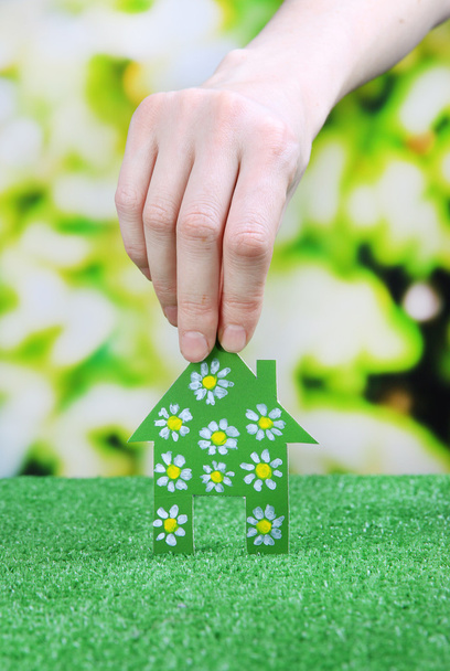 papier huisje in hand op groen gras op lichte achtergrond - Foto, afbeelding