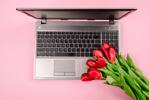 Boeket rode tulpen op roze papieren achtergrond met laptop op werkplaats. Sjabloon voor reclame of visualisatie van blog met kopieerruimte voor tekst. Een visitekaartje. Vakantie certificaat. Banner. - Foto, afbeelding