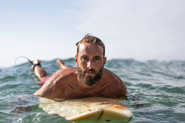 Young hipster man swimming on the surfboard into the sea water waiting for a big wave - Cool guy having fun doing extreme sport - Adventure and freedom concept doing water sports - Focus on his face - Фото, изображение