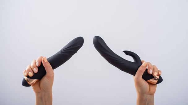 A faceless woman holds two black dildos on a white background - Fotografie, Obrázek