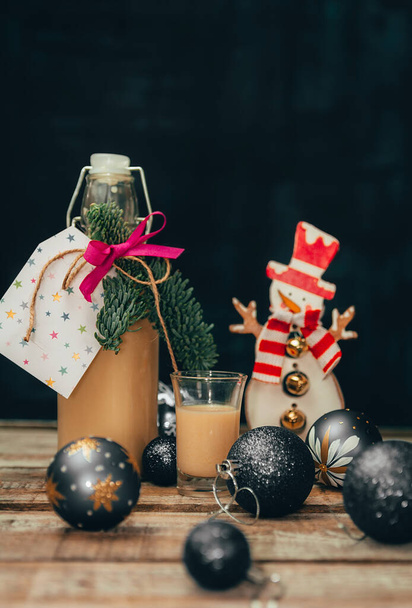 Домашня алкогольна яєчна рідина з баночкою, свічкою, сніговиком та різдвяним м'ячем на дерев'яному столі
 - Фото, зображення