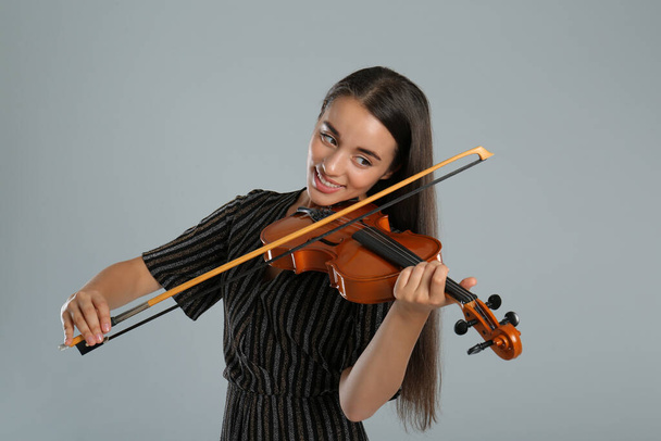 Beautiful woman playing violin on grey background - Foto, afbeelding