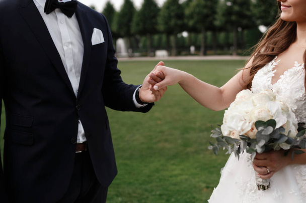 Весільна фотографія подружньої пари, що тримає руки на відкритому повітрі. наречена тримає в руці букет білих квітів. день весілля
. - Фото, зображення