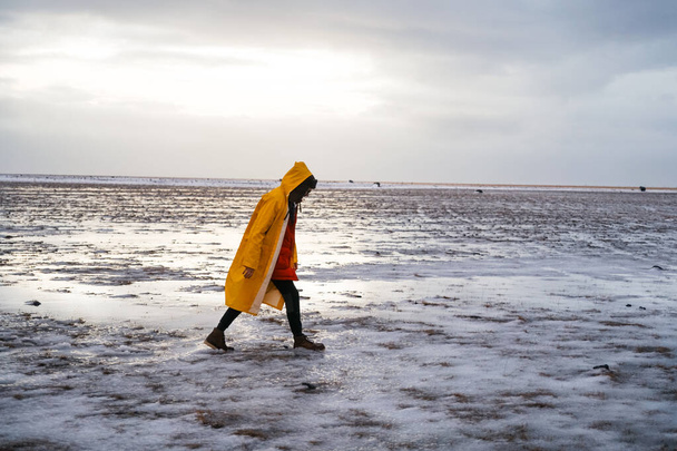 un homme en imperméable jaune traverse un champ neigeux sous la pluie. Nature sauvage intacte de l'Islande en hiver. Voyages - Photo, image