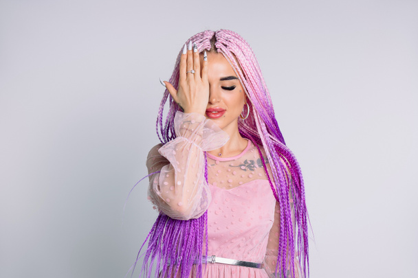 Hipster girl with long pink hair posing with closed eyes for the camera, covering her eyes with her hand. High quality photo - Photo, image