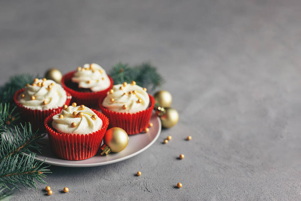 Tasty cupcakes decorated with golden pearls and spruce branches on a grey background. Sweets for the celebration Christmas.  Place for text. - Фото, изображение