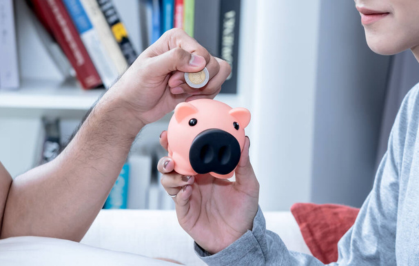 A man putting money into a piggy bank, withe blur background, concept to couple and saving money for the future - Photo, Image