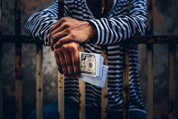 Преступники-мужчины, пойманные в грязной клетке по обвинению в подделке банковского доллара, в котором он держал фальшивую банкноту в руке, к концепции финансовых преступлений. - Фото, изображение