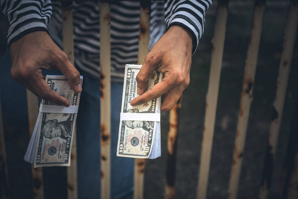 Άντρες εγκληματίες πιάστηκαν σε ένα βρώμικο κλουβί με την κατηγορία της παραχάραξης ενός δολαρίου, στο οποίο κρατούσε το πλαστό χαρτονόμισμα στο χέρι του, στην έννοια του οικονομικού εγκλήματος.. - Φωτογραφία, εικόνα