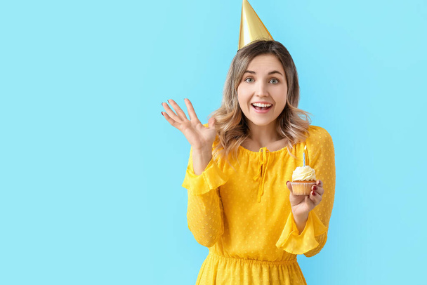 Beautiful young woman with birthday cupcake on color background - 写真・画像