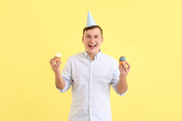 Молодий чоловік з кексами на день народження на кольоровому фоні
 - Фото, зображення