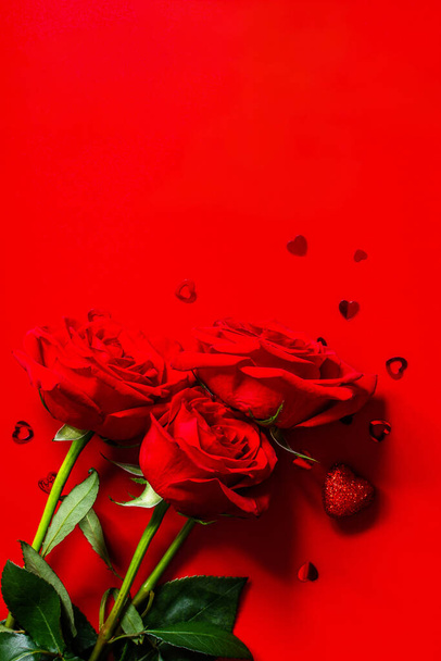 Strauß roter Rosen und Dekor in Herzform auf rotem Hintergrund. Draufsicht, flache Lage. Kopierraum. - Foto, Bild