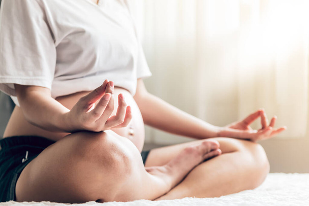 Mujeres embarazadas sentadas y practicando yoga En la cama blanca, es una práctica de meditación para relajar la mente, concepto a la madre y saludable. - Foto, Imagen