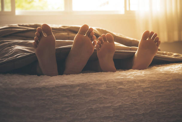 I piedi dell'amante uscirono dalla coperta, in cui erano entrambi distesi su un letto bianco, alla luce del mattino, alle coppie e al concetto di giorno di San Valentino.. - Foto, immagini