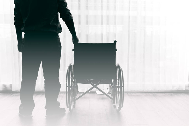 Человек, стоящий и инвалидное кресло в больнице с белыми занавесками заднего плана, к концепции здоровья. - Фото, изображение