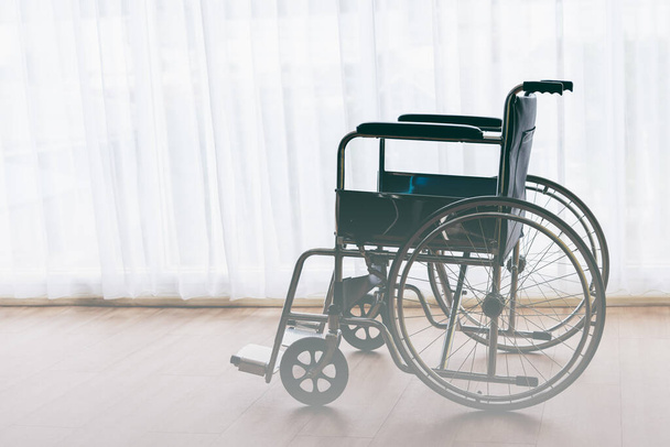 Инвалидная коляска, припаркованная на деревянных полах с белыми шторами на фоне, согласно концепции здоровья. - Фото, изображение