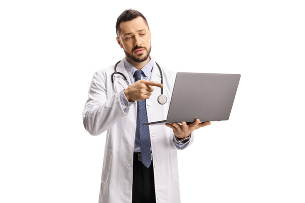 Médico varón sosteniendo una computadora portátil y apuntando a la pantalla aislada sobre fondo blanco - Foto, imagen