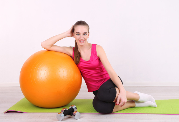 Young beautiful fitness girl exercising with orange ball and dumbbells in gym - Photo, image