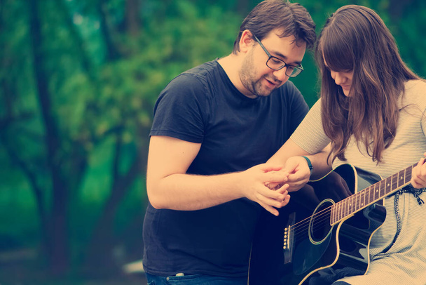 Brother teaching sister to play guitar in nature - Photo, Image