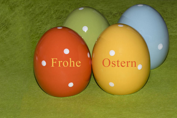 Quattro colorate uova di Pasqua in ceramica davanti a uno sfondo verde con saluti pasquali in tedesco - Foto, immagini