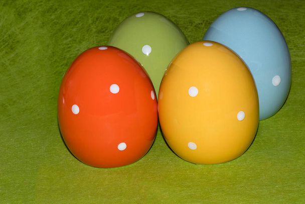 Cuatro coloridos huevos de Pascua de cerámica frente a un fondo verde con lugar para saludos de Pascua - Foto, imagen