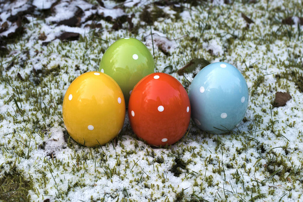 Húsvét, színes kerámia húsvéti tojások, amelyek állnak a fű és a hó. - Fotó, kép