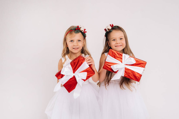 two little girls in white dresses with Christmas gifts on a white background smile. - Zdjęcie, obraz