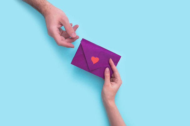 woman hand gives an envelope with a heart to a man in hand on a pink background. valentines day. - Fotoğraf, Görsel