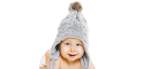 Portrait of happy smiling baby wearing a winter knitted gray hat over a white background - Zdjęcie, obraz