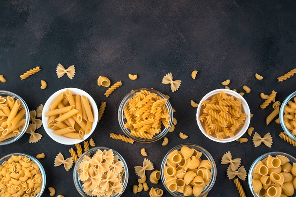 Bowls of pasta of different varieties on a dark concrete background. - Фото, зображення