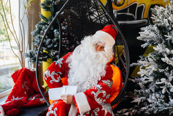 Santa Claus is sitting on a chair and reading letters. - Fotografie, Obrázek