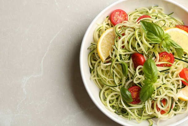 Delicious zucchini pasta with cherry tomatoes, lemon and basil on light grey table, top view. Space for text - Fotó, kép