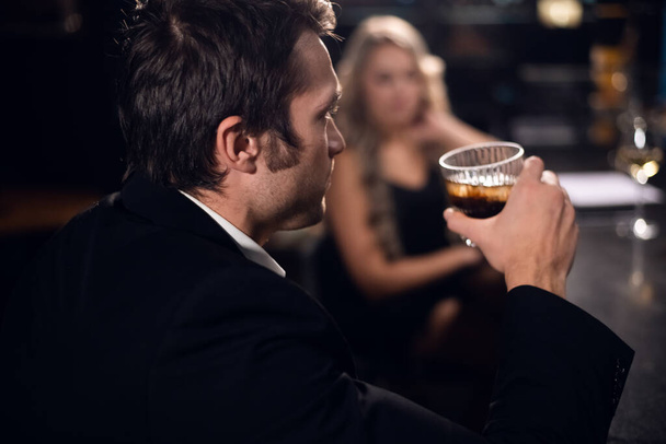 mladý muž v obleku pije whisky s kolou a ledem v baru v nočním klubu - Fotografie, Obrázek