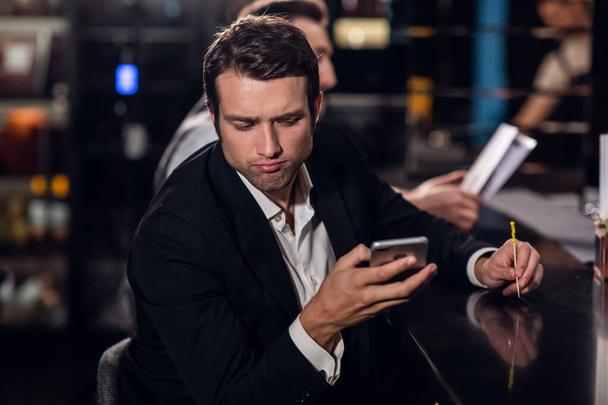 a young man reads a message on his phone, sits in a bar - Фото, изображение