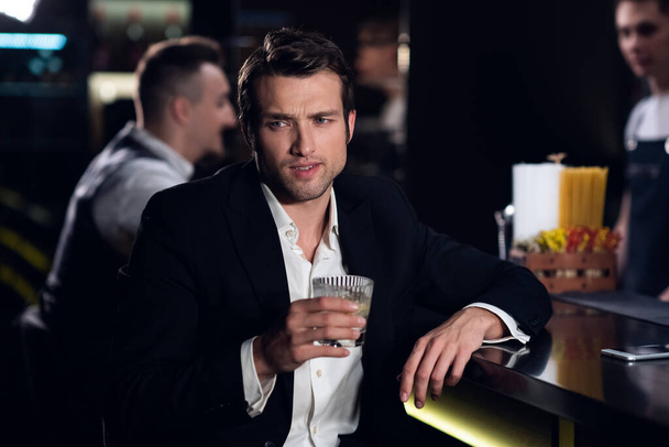 portrait d'un jeune homme vêtu d'une chemise et d'une veste au bar avec un cocktail à la main - Photo, image