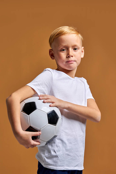sportive boy in sportswear holding soccer ball, posing at studio - Фото, зображення