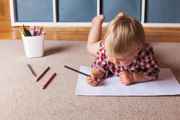 Dziecko rysuje ołówkami w albumie, leżąc na podłodze Koncepcja gier edukacyjnych, nauki pozalekcyjnej. - Zdjęcie, obraz