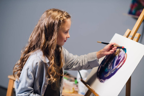 Una niña de vacaciones en su habitación dibuja una pintura al óleo. Una artista apasionada por su hobby. - Foto, Imagen