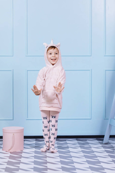 Sonriendo hermosa niña en traje rosa unicornio es sonreír y divertirse en un fondo de pared azul. feliz infancia - Foto, imagen