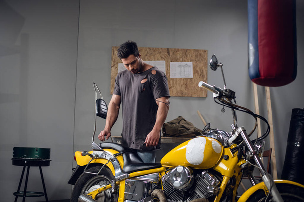 A young mechanic tuning a motorcycle in an auto repair shop. Hobbies and work activity. - Photo, Image