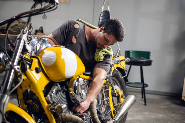Private vehicle repair shop. Tuning a yellow chopper by a young mechanic. - Photo, Image