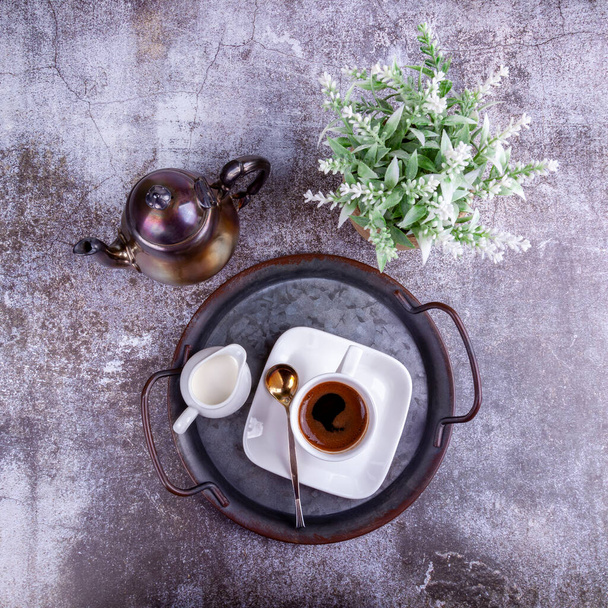 Espresso coffee in white porcelain cup and cream in a portioned jug on vintage metal tray - 写真・画像