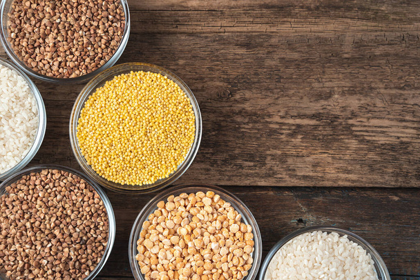 Buckwheat, rice, millet, peas in round bowls on a wooden background. - Φωτογραφία, εικόνα