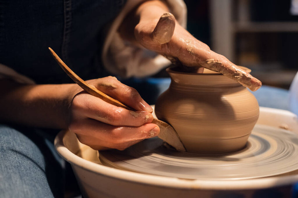 close-up van de handen van een pottenbakker bij het beeldhouwen van een vaas uit klei op een pottenbakkerswiel in de werkplaats. - Foto, afbeelding