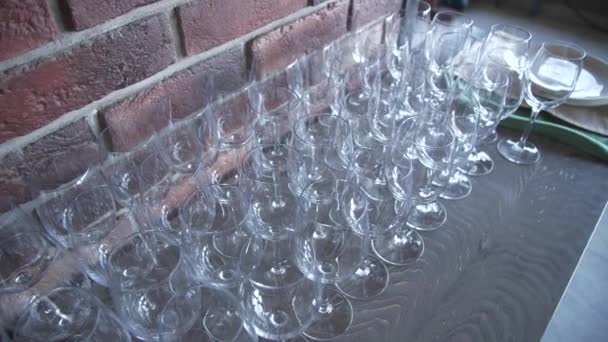 Krystalicznie czyste kieliszki do wina świecą na stole pod ceglaną ścianą. Stolik obsługowy w kawiarni - Materiał filmowy, wideo