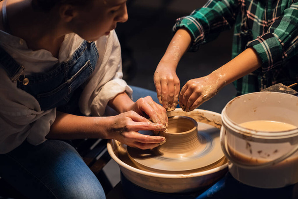 una joven madre enseña a su hijo la artesanía de cerámica familiar en un taller. - Foto, Imagen