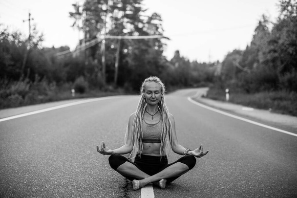 ヨガの女性瞑想は、国の道路の真ん中に座っている。白黒写真. - 写真・画像