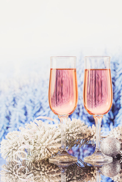 Two glasses of rose champagne and Christmas or New Year decoration with winter snowy forest bokeh as a background. Romantic dinner. Winter holiday concept. - Zdjęcie, obraz